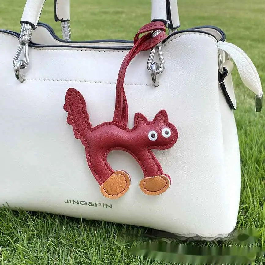 Red leather mini cat bag charm with white eyes and tan paws attached to a white handbag for trend den style Wine Red