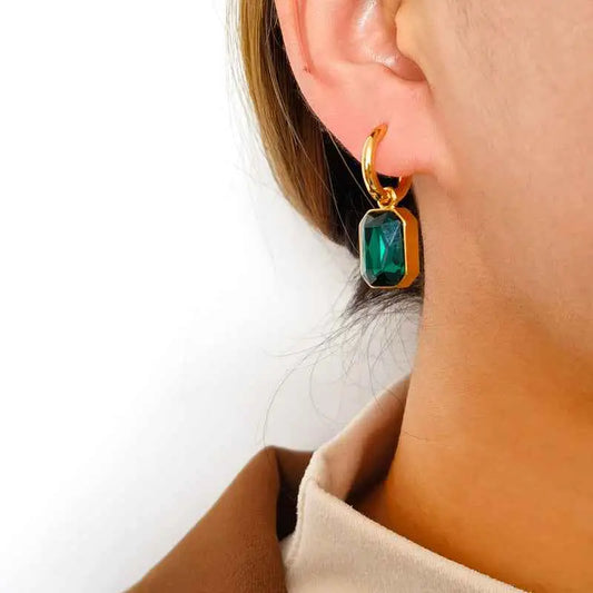A female wearing a gold earring with a green gemstone