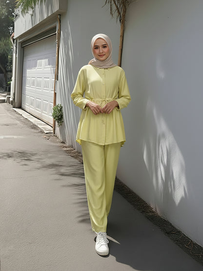 Woman in a light green outfit standing against a white wall. Bright Yellow