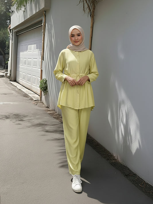 Woman in a light green outfit standing against a white wall. Bright Yellow