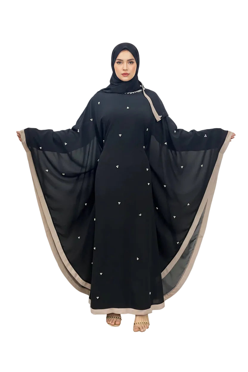 Black abaya with beige trim draped over a person against a white wall. Black