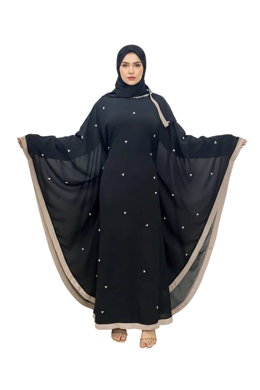 Black abaya with beige trim draped over a person against a white wall. Black
