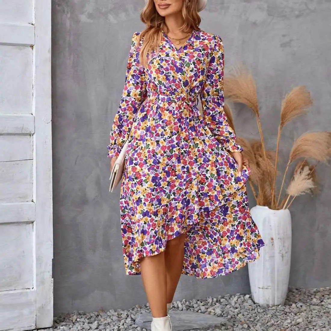 A woman wearing a vibrant floral ruffled long sleeve dress with asymmetrical hemline and fitted waistband Purple Pink