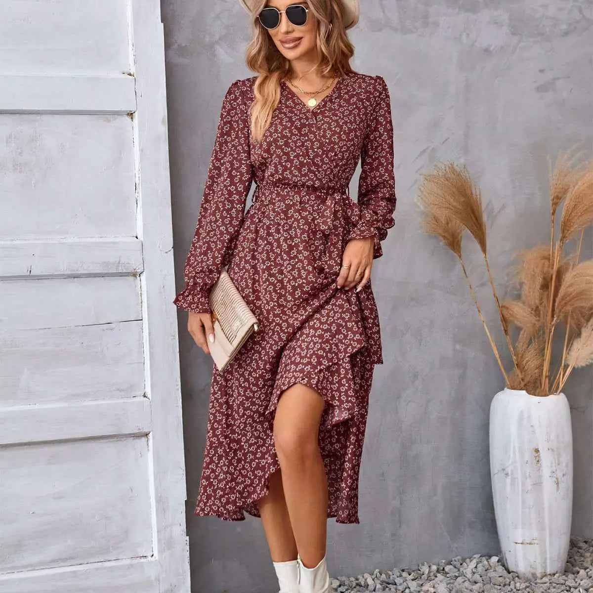 A woman wears a maroon floral ruffled long sleeve wrap dress with an asymmetrical hemline
