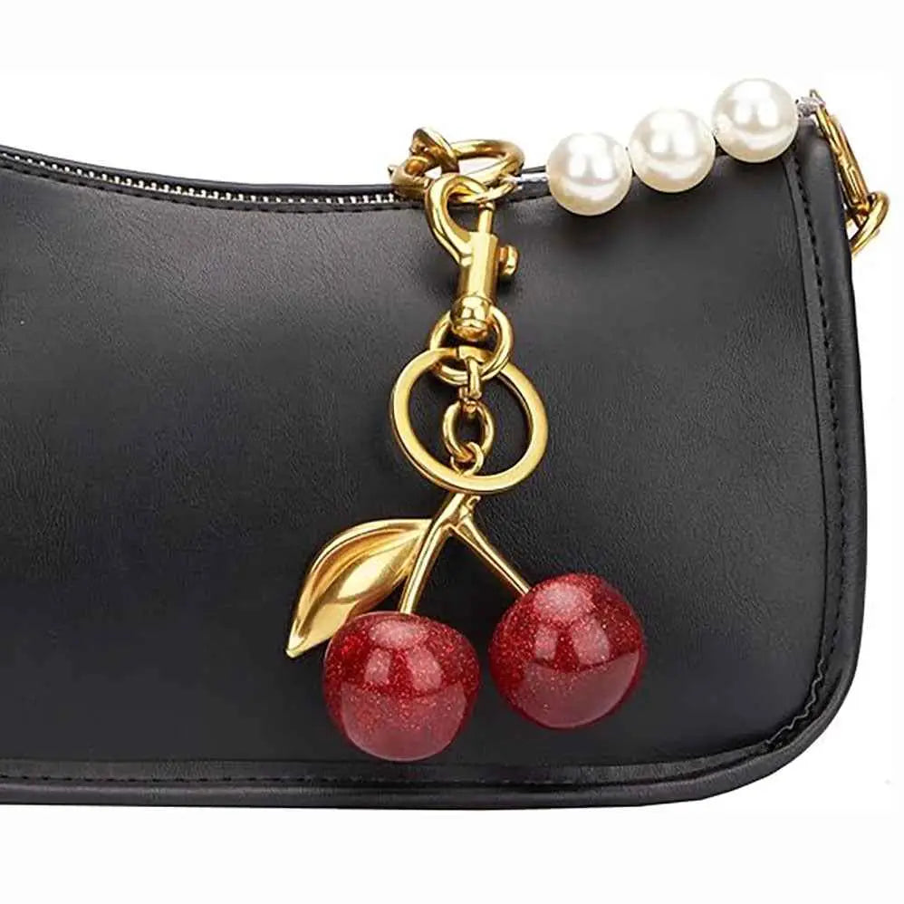 A glossy cherry bag charm keychain featuring zinc alloy gold accents and a pearl strap attached to a black leather bag