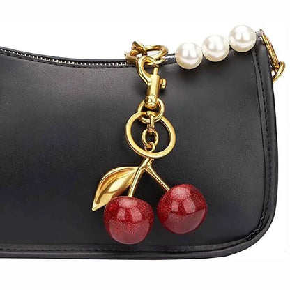A glossy cherry bag charm keychain featuring zinc alloy gold accents and a pearl strap attached to a black leather bag