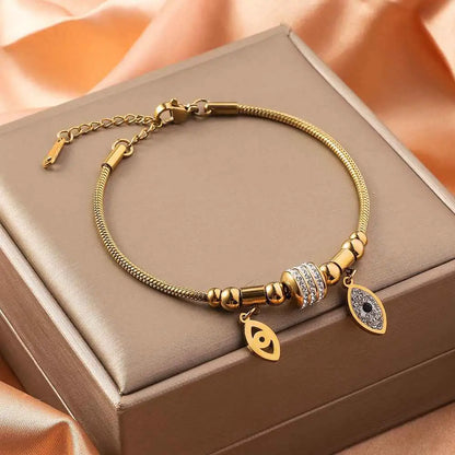 Gold shell charm bracelet in gold-toned titanium steel with rhinestone bead and eye-shaped charms including black pupil Devil Eye