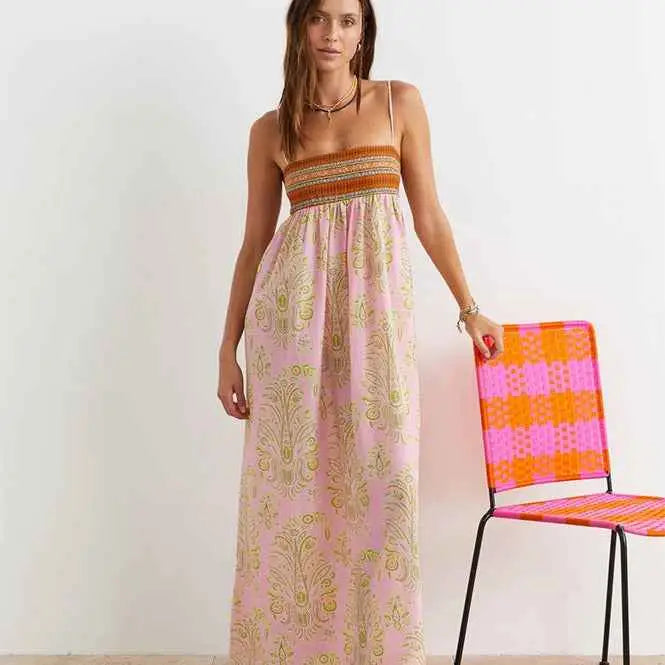 A flowing pink printed large swing dress with gold paisley patterns and an orange-brown smocked bodice
