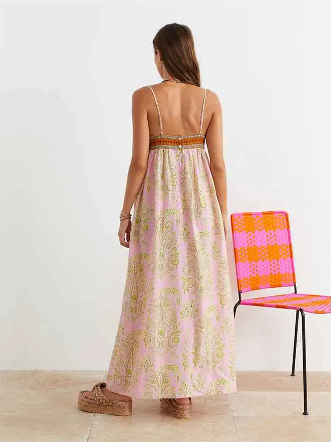 A woman wearing a light pink printed large swing dress with gold paisley patterns and thin spaghetti straps