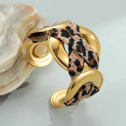Gold-toned cuff bracelet with leopard ribbon fabric woven through its polished geometric metal bangle structure