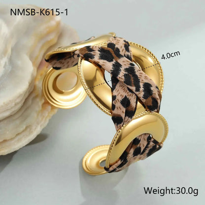 Gold-toned cuff bracelet with leopard ribbon geometric fabric woven through its curved metallic structure NMSBK6151