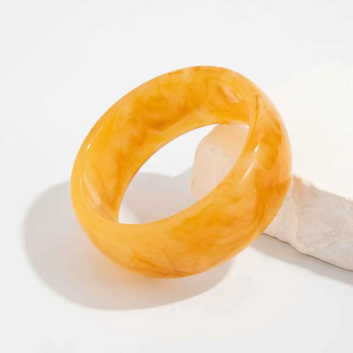 A smooth glossy amber marbled translucent resin statement bangle featuring swirling golden patterns from trend den Beige