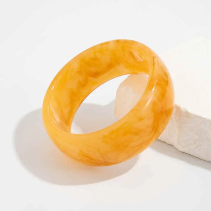 A smooth glossy amber marbled translucent resin statement bangle featuring swirling golden patterns from trend den Beige