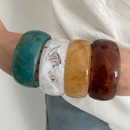 Four marbled translucent resin statement bangles in teal white swirls amber and deep brown from trend den