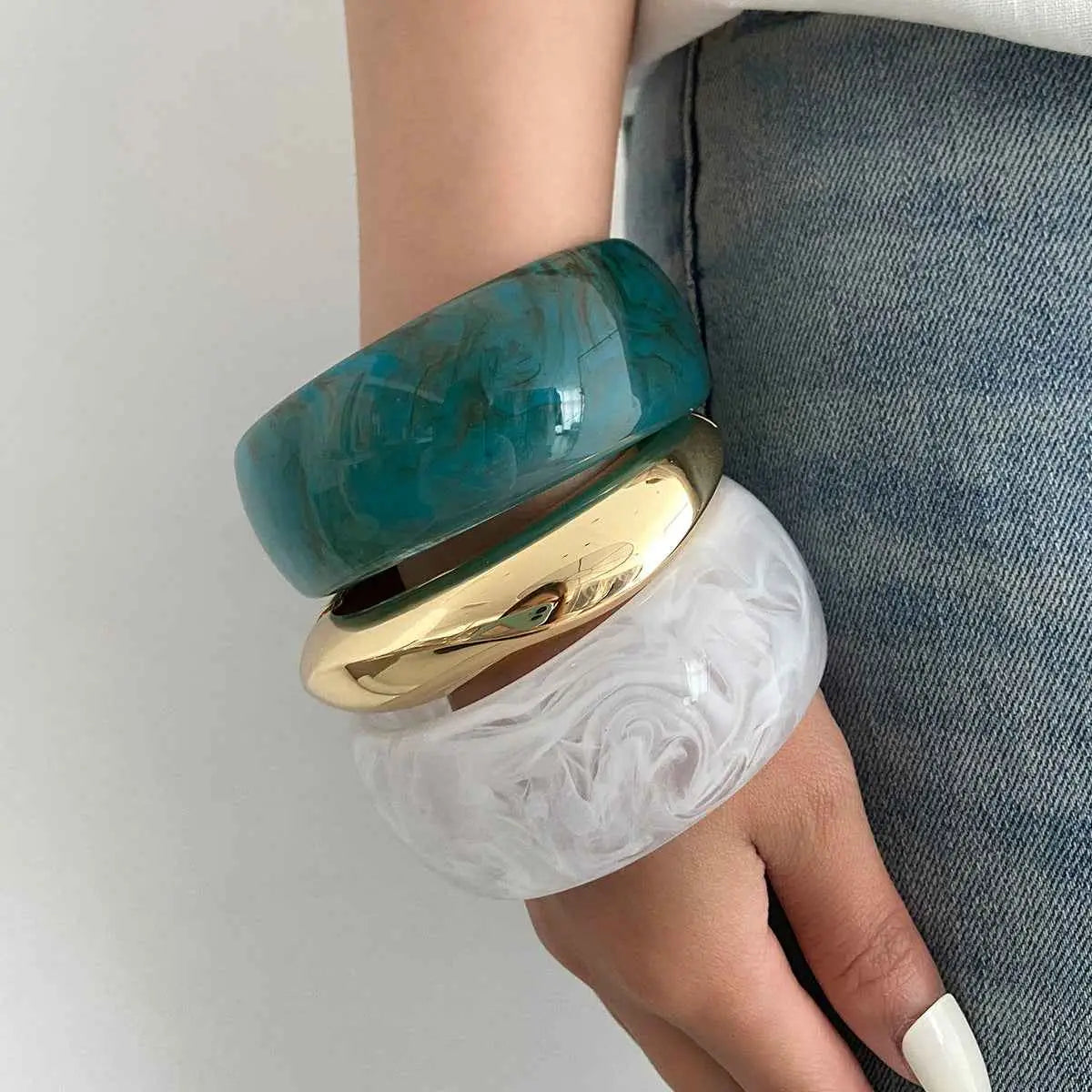 Stacked bangles featuring a glossy teal marbled top gold band and translucent white swirl marbled translucent resin design
