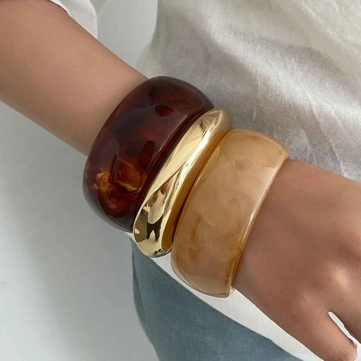 Three stacked marbled translucent resin bangles in glossy tortoiseshell amber and gold tone from trend den