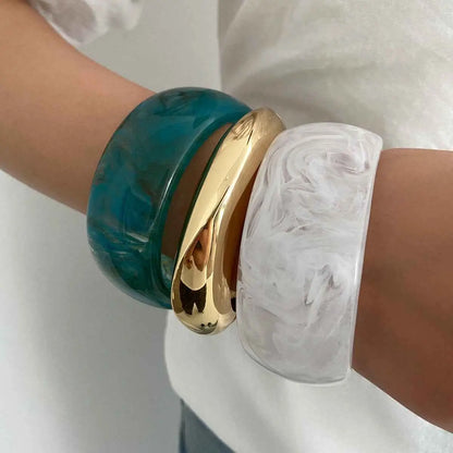 Three stacked bangles on wrist featuring a marbled translucent resin white bangle teal translucent and polished gold designs