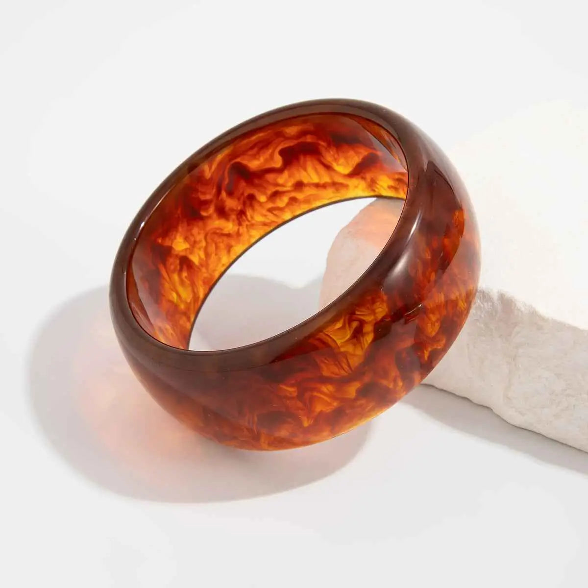 Glossy amber tortoiseshell marbled translucent resin statement bangle with swirling orange and brown patterns from trend den Brown