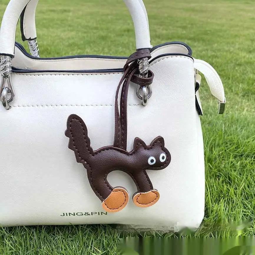 Mini cat bag charm brown leather with white eyes and tan paw pads attached to white handbag by matching strap trend den Dark Brown