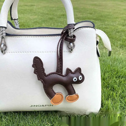 Mini cat bag charm brown leather with white eyes and tan paw pads attached to white handbag by matching strap trend den Dark Brown
