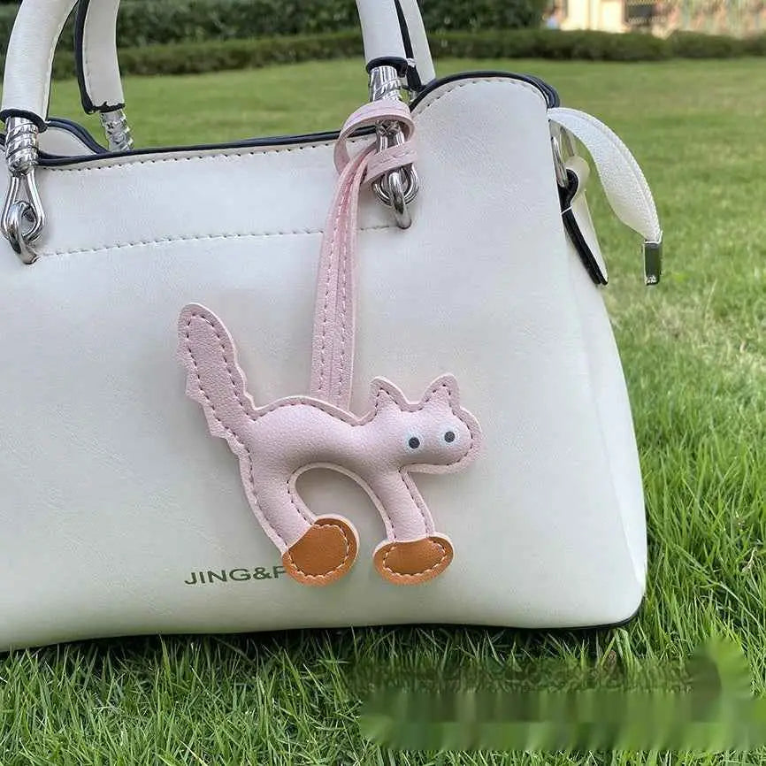Mini cat bag charm in delicate pink leather with tan paw pads hanging from a white handbag by trend den Light Pink