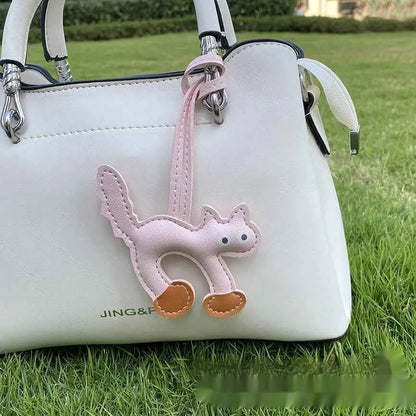 Mini cat bag charm in delicate pink leather with tan paw pads hanging from a white handbag by trend den Light Pink