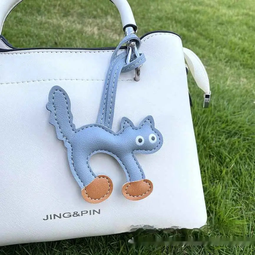 Light blue leather mini cat bag charm with tan paw pads and stitched details attached to a white handbag trend den accessory Peacock Blue