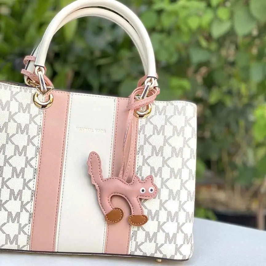 A pink and white michael kors mini cat bag with soft leather handles and a playful cat bag charm trend den accessory Pink