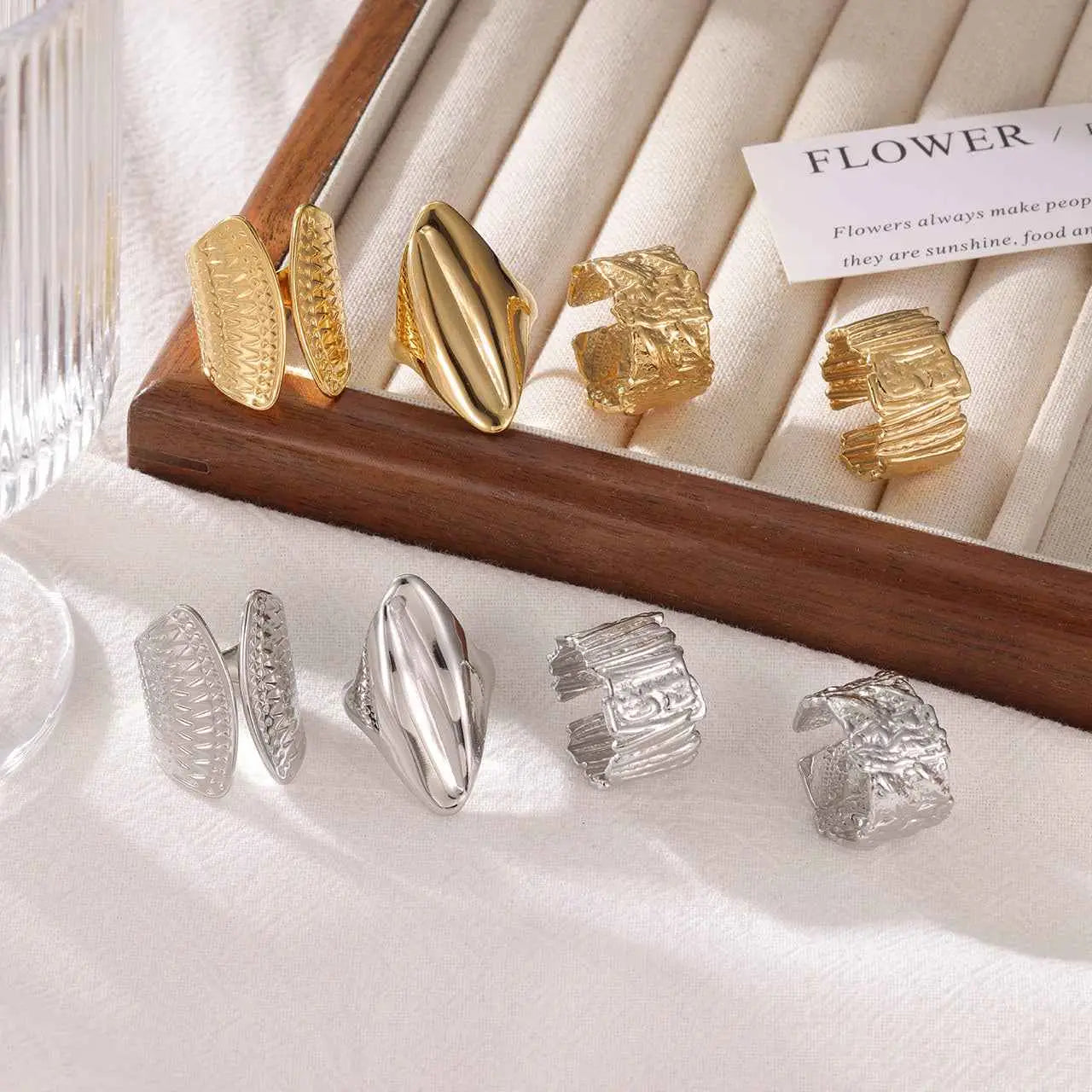 Minimalist geometric adjustable rings in gold and silver titanium steel with textured sculpted designs in a wooden tray