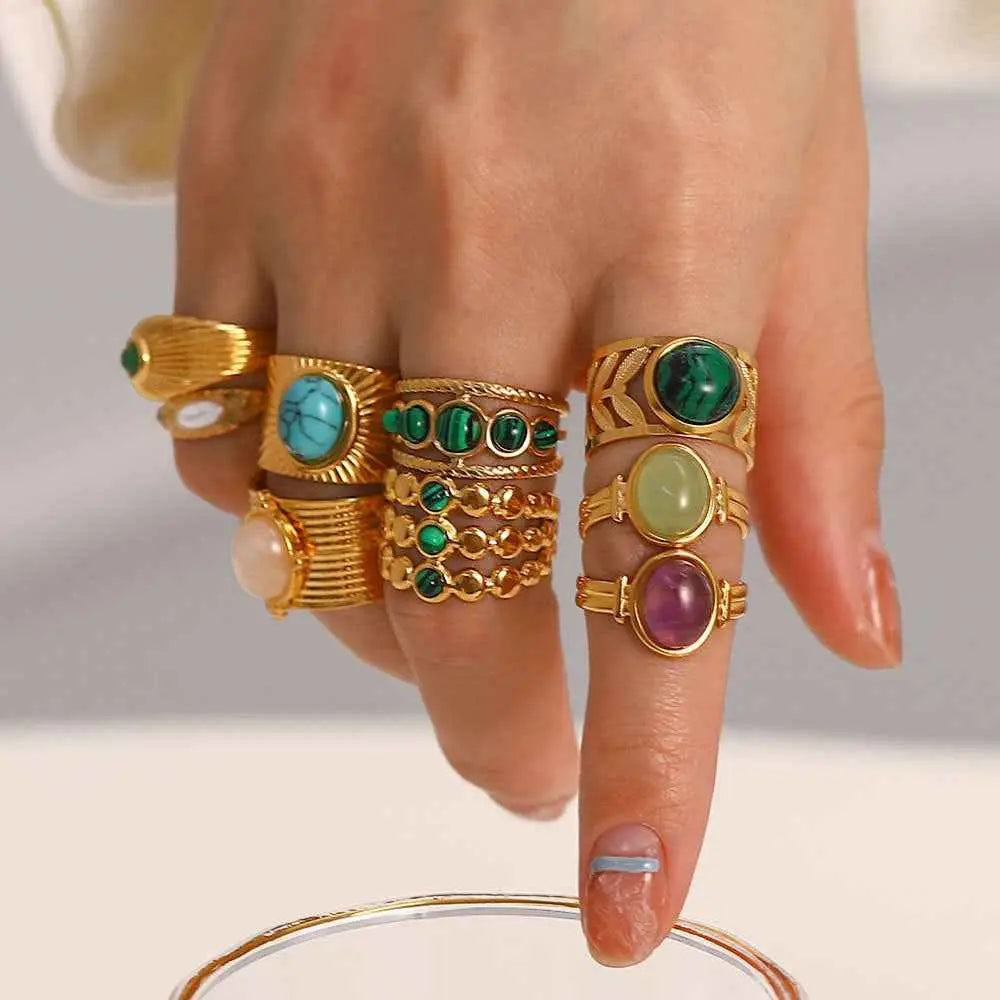 A hand wearing multiple gold-toned natural stone adjustable zircon rings featuring turquoise malachite and amethyst gemstones