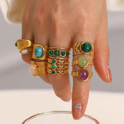 A hand wearing multiple gold-toned natural stone adjustable zircon rings featuring turquoise malachite and amethyst gemstones