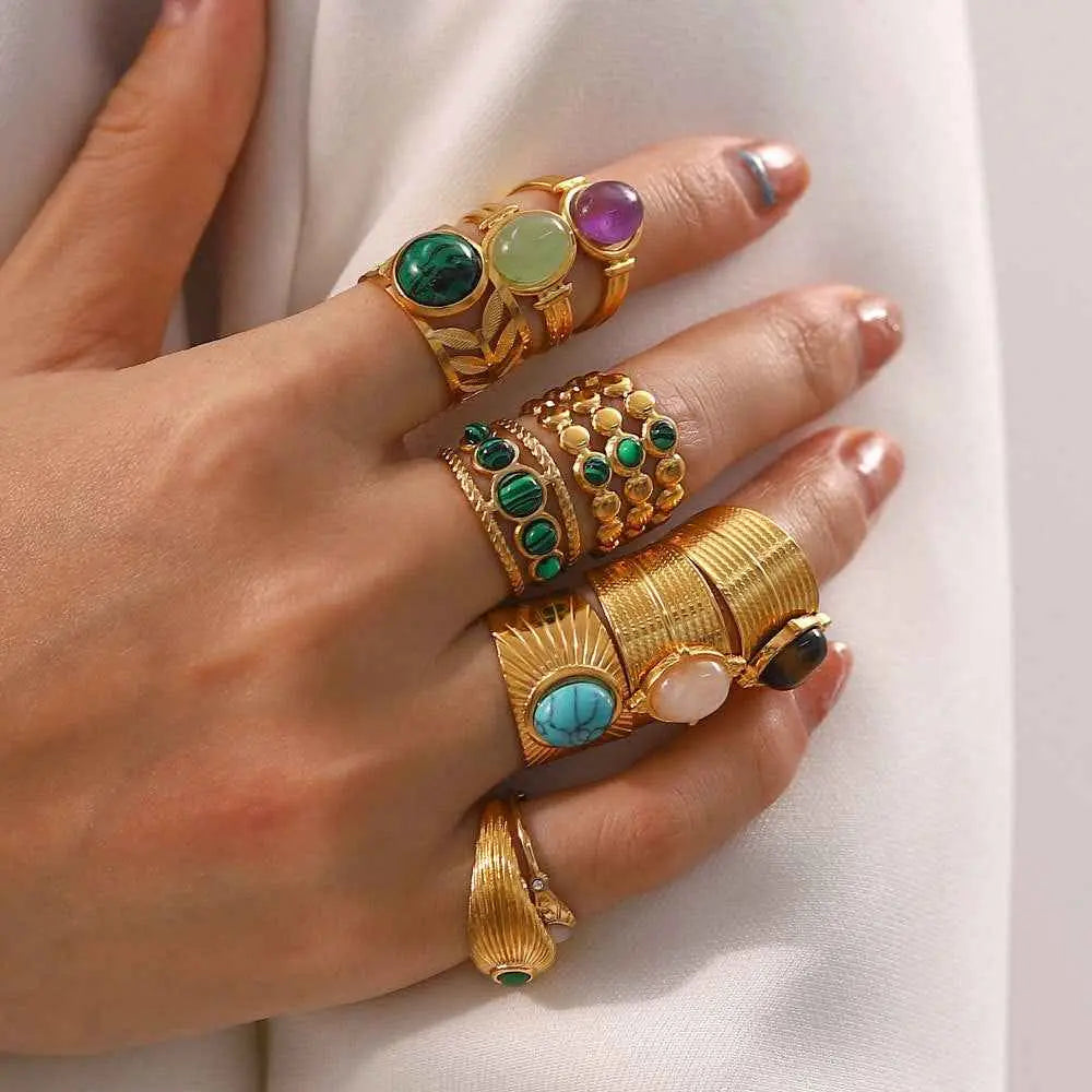 A hand wearing multiple natural stone adjustable zircon rings featuring green emerald, blue turquoise, and purple amethyst gemstones