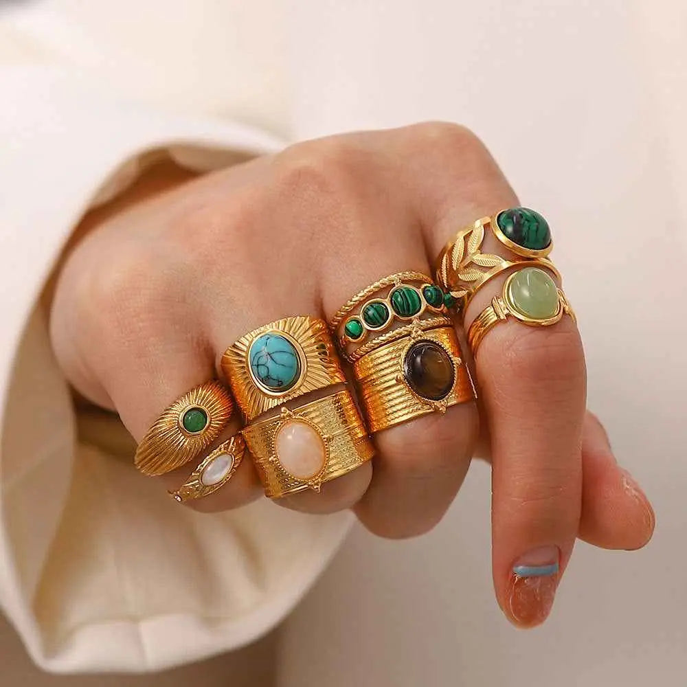 A hand wearing multiple natural stone adjustable zircon rings featuring turquoise malachite and opal gemstones