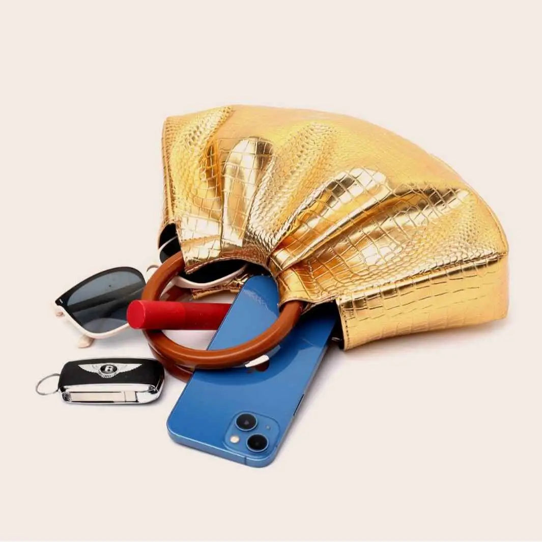 A shiny gold crocodile-patterned pleated shell-shaped handbag with a curved brown handle from trend den