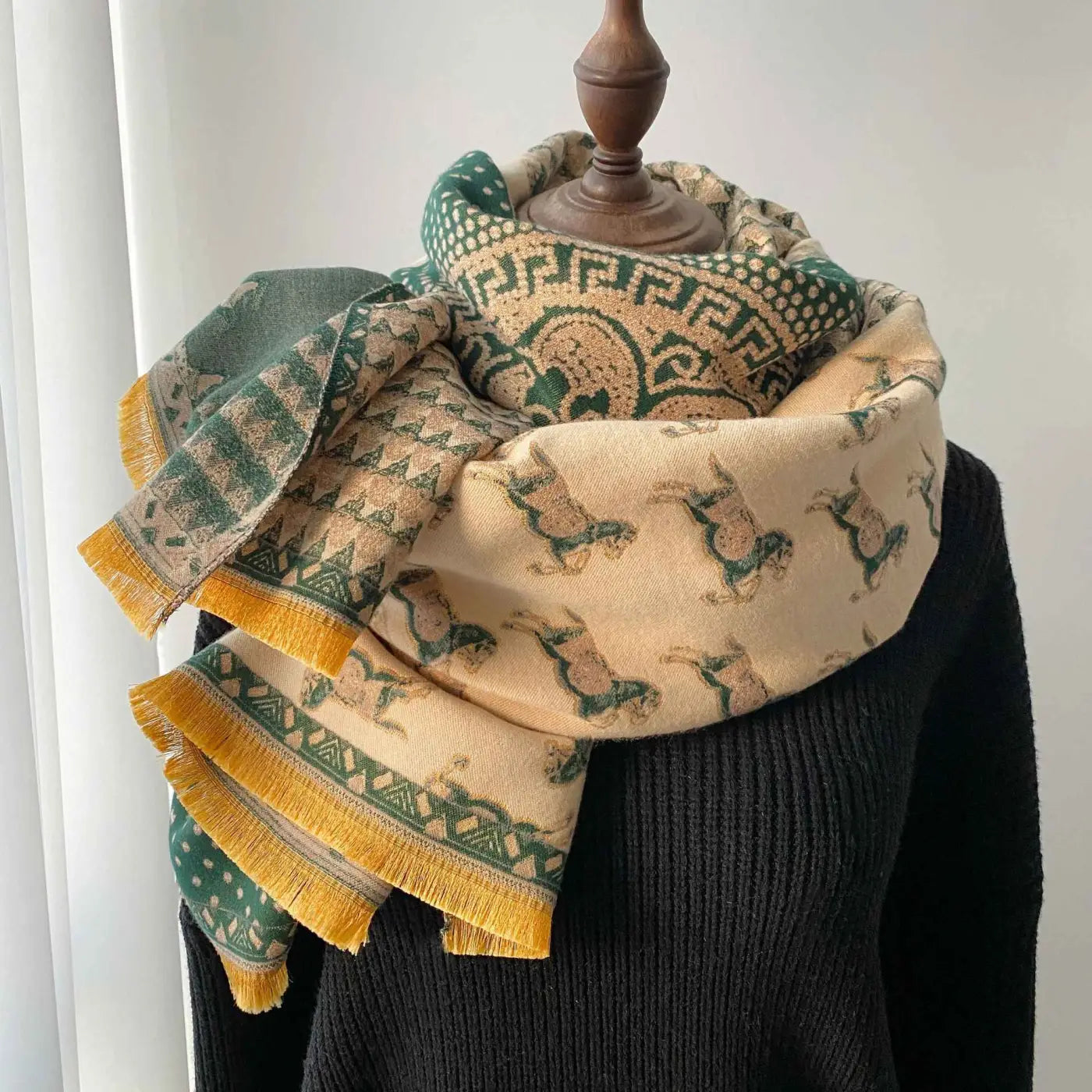 A cozy retro carriage jacquard scarf in cream and green with mustard yellow tassels draped on a mannequin