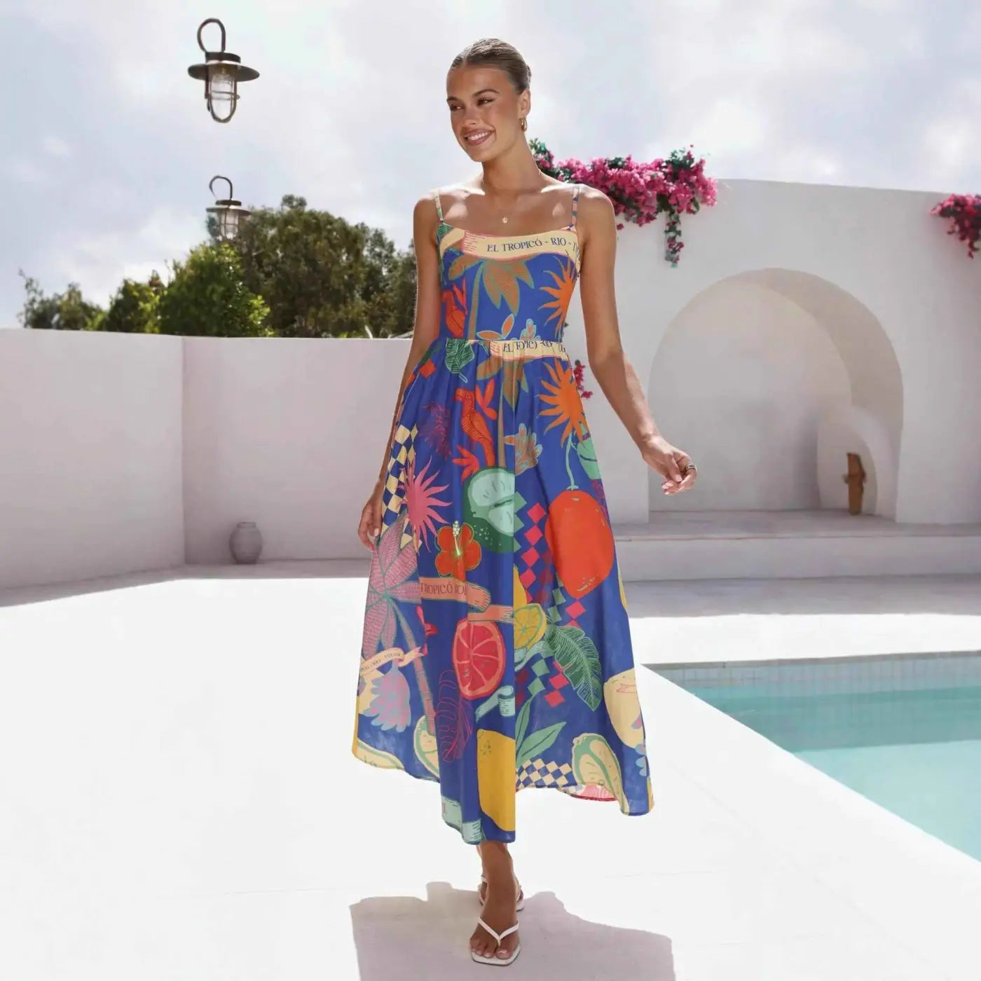 A vibrant blue south african linen print slip dress with colorful tropical fruit and floral patterns and spaghetti straps