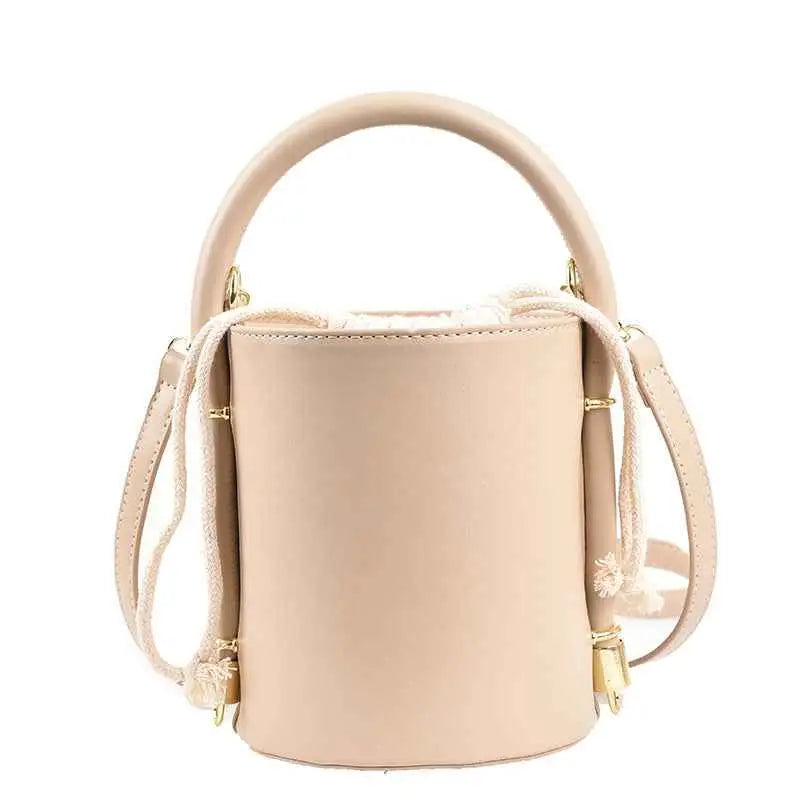 Beige leather structured cylinder bucket bag with rounded top handle, adjustable strap, gold hardware, and tassel accents from trend den Beige