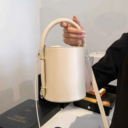 Cream-colored leather structured cylinder bucket bag with curved top handle and gold-tone hardware from trend den